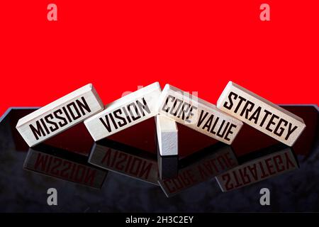 MISSIONE, VISIONE, VALORE DI BASE, STRATEGIA Un simbolo dei nostri valori di base. Parole concettuali su blocchi di legno su sfondo nero e rosso. Concetto di busines Foto Stock