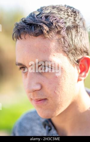 Primo piano di ragazzo di latino dai capelli scuri con i capelli scuri adolescente allegro e sorridente. Immagine all'aperto con sfondo sfocato. Foto Stock