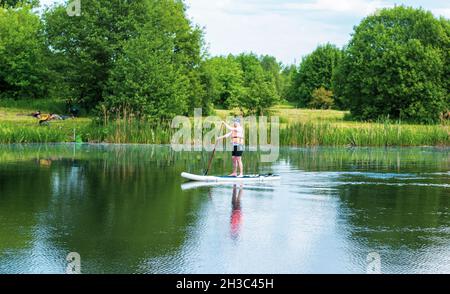 Un uomo su una tavola con una pagaia nel lago, SUP. Giorno d'estate . 5 giugno 2021 Minsk, Bielorussia. Fiume Svisloch Foto Stock