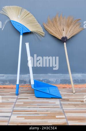 La scopa a spazzatura doppia e la paletta di plastica sono appoggiate contro la parete laterale della casa per l'uso all'esterno della casa, vista frontale per la copia spa Foto Stock