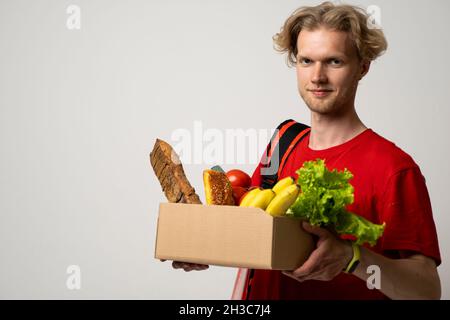 Ritratto di sorridente bell'uomo di consegna che tiene la scatola della drogheria di carta con un drogheria isolato su sfondo bianco. Foto Stock