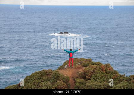 Felice turista in piedi su una scogliera di fronte al mare con le braccia aperte Foto Stock