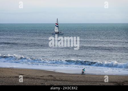 Due persone che camminano sulla spiaggia di Seabright con uno yacht che naviga al largo della costa di Santa Cruz California ; USA Foto Stock