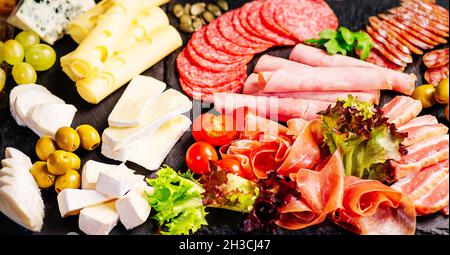 Salumi, antipasti con assortimento di salumi, formaggi, camembert e olive su tavola di legno. Vari tipi di carne e salsicce su legno Foto Stock