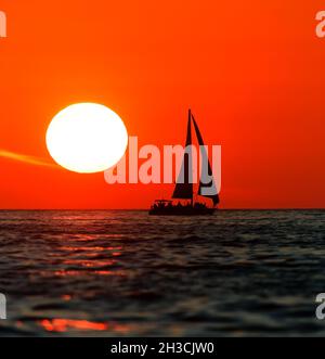 Una barca a vela sta navigando lungo l'oceano contro Un vivace rosso tramonto colorato in verticale immagine formato Foto Stock