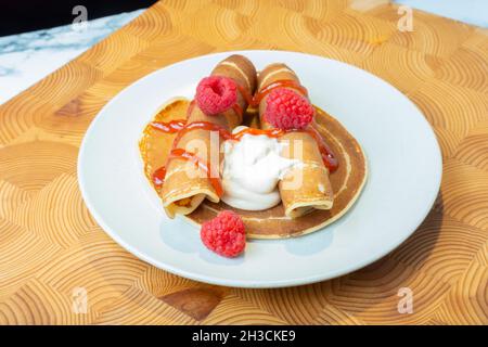 Helsinki / Finlandia - 27 OTTOBRE 2021: Un piatto di soffici pancake norvegesi con panna montata caramellata e confettura di lamponi sul lato. Foto Stock