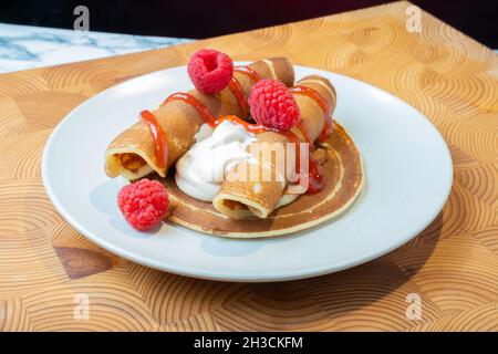 Helsinki / Finlandia - 27 OTTOBRE 2021: Un piatto di soffici pancake norvegesi con panna montata caramellata e confettura di lamponi sul lato. Foto Stock