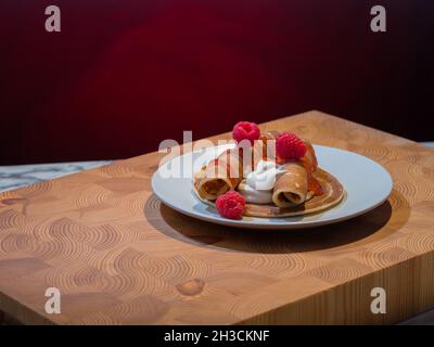 Helsinki / Finlandia - 27 OTTOBRE 2021: Un piatto di soffici pancake norvegesi con panna montata caramellata e confettura di lamponi sul lato. Foto Stock