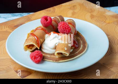 Helsinki / Finlandia - 27 OTTOBRE 2021: Un piatto di soffici pancake norvegesi con panna montata caramellata e confettura di lamponi sul lato. Foto Stock