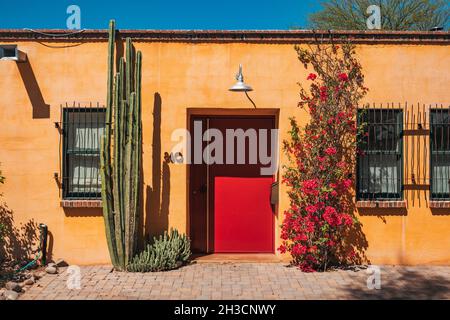 Una grande porta di metallo rosso colpisce un contrasto con i muri gialli in adobe (pietra fangosa) di una casa a Barrio Viejo, Tucson, AZ Foto Stock