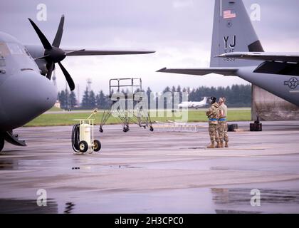 Due manutentori con il 374° Maintenance Group osservano il funzionamento del motore C-130J Super Hercules mentre un C-12J Huron atterra sulla linea di volo alla base aerea di Yokota, Giappone, 9 settembre 2021. Il 374th MXG mantiene gli aerei C-130J, C-12J e UH-1N che supportano l'airlift intra-teatro e il trasporto di visitatori distinto per le forze aeree del Pacifico. (STATI UNITI Air Force foto di Tech. SGT. Amanda Sampson) Foto Stock