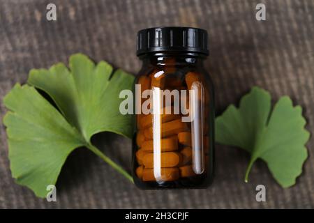 Ginkgo biloba pills .Brown vaso di vetro con pillole con estratto di ginkgo e foglie di ginkgo su sfondo di legno . Medicina alternativa e omeopatia Foto Stock