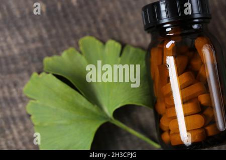 Ginkgo biloba pills .Brown vaso di vetro con pillole omeopatiche con estratto di ginkgo e foglie di ginkgo su sfondo di legno . Medicina alternativa e. Foto Stock