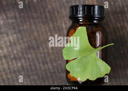 Ginkgo biloba pills .Brown vaso di vetro con pillole omeopatiche con estratto di ginkgo e foglie di ginkgo su sfondo di legno . Medicina alternativa e. Foto Stock