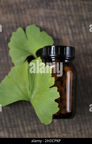 Ginkgo biloba pills .Brown vaso di vetro con pillole omeopatiche con estratto di ginkgo e foglie di ginkgo su sfondo di legno .Natural bio farmaci a base di erbe. Foto Stock