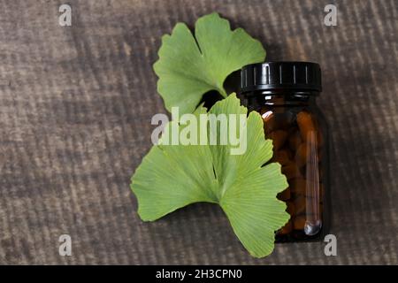 Ginkgo biloba pills .Brown vaso di vetro con pillole omeopatiche con estratto di ginkgo e foglie di ginkgo su sfondo di legno . Medicina alternativa e. Foto Stock