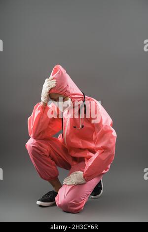 Medico che indossa i DPI e la maschera tenendo la testa in una mano con un gesto triste Foto Stock