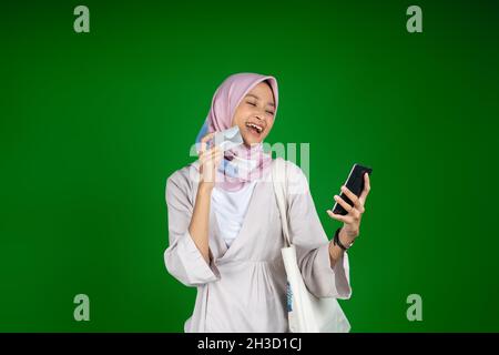 Donna in hijab ridendo mentre usando il telefono cellulare mentre tiene la carta atm Foto Stock