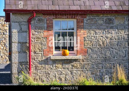 Bella vista closeup della tipica campagna irlandese casa facciata con zucca sul davanzale della finestra in luminoso giorno d'autunno soleggiato. Halloween 2021 decorazioni Foto Stock