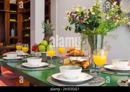 Tavolo da pranzo con servizio di prima colazione, succhi di frutta, frutta e dolci pronti a mangiare in un appartamento in affitto per le vacanze Foto Stock