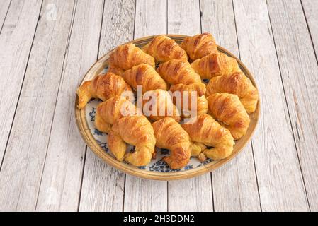 Piatto blu ripieno d'oro con mini croissant al burro su tavolo di legno chiaro Foto Stock