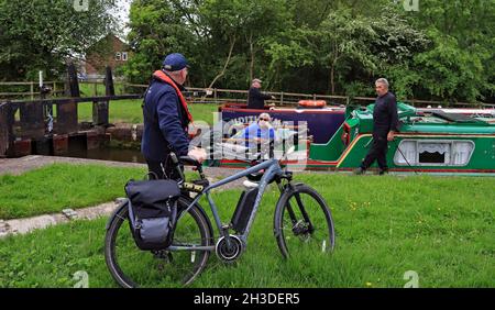 Un equipaggio di barca stretto chiacchiera con un portiere volontario mentre lavorano giù il volo di Wigan, il volontario sta usando una bici per viaggiare tra le serrature. Foto Stock