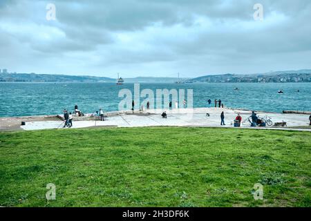 Una nave enorme nel ponte di bosforo istanbul vicino al distretto di sarayburnu con molte persone a piedi e la pesca in riva al mare durante il tempo coperto Foto Stock