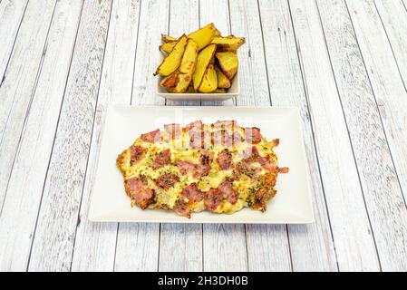 Schnitzel di vitello con un sacco di formaggio fuso e pezzi di pancetta fritta e guarnire di patate arrosto tagliate a spicchi Foto Stock