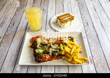 Menu milanese di vitello con fette di parmigiano, salsa di pesto, guarnire con patatine fritte, succo d'arancia e torta di carote Foto Stock