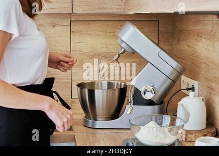 Donna che cucinano torta fatta in casa. Mixer elettrico e ingredienti alimentari in cucina. Elettrodomestici da cucina Foto Stock
