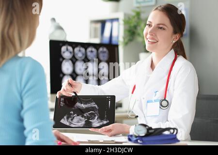 Ritratto di ginecologo sorridente che tiene l'immagine ecografica e mostra bambino piccolo Foto Stock