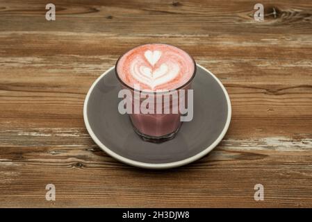 Latte rosa servito da un barista che attira i cuori su un tavolo di legno Foto Stock