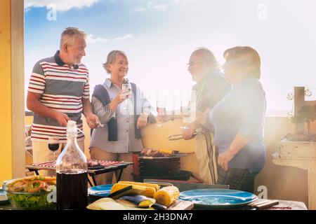 Gruppo di persone anziane si divertono nella frathenship all'aperto cucinare un barbecue tutti insieme. Gli amici delle coppie anziane godono di tempo libero mangiando e bevendo e ce Foto Stock