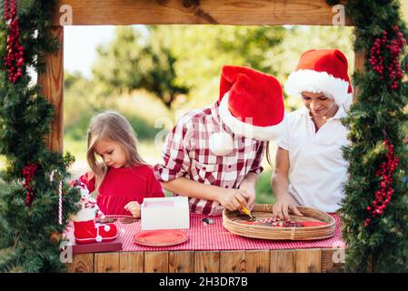 Bambini felici che si preparano per Natale. Due ragazzi e bambina in santa Hat, biscotti color pan di zenzero fuori divertirsi. I bambini decorano pan di zenzero uomo. H Foto Stock