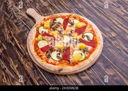 Pizza vegana con formaggio di patate, pepe rosso arrostito, pezzi di ananas, funghi e fette di cetriolo Foto Stock