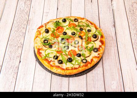 Pizza vegana con formaggio di patate con rucola, fette di melanzana, fette di olive nere, fette di pomodoro ciliegia, fette di zucchine e pomodoro Foto Stock