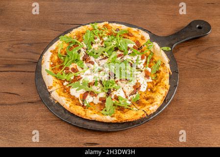 Pizza vegana con formaggio di patate, rucola, uvetta, pomodoro disidratato e vassoio nero Foto Stock