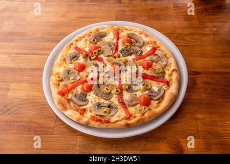 Pizza vegana con peperoni arrostiti, formaggio di patate, pomodori ciliegini interi, fette di funghi, cipolla bianca, olive verdi e salsa di pomodoro Foto Stock