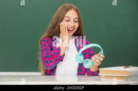 sorprendo ragazza teen tenere cuffie moderne in high school a lavagna, scuola Foto Stock