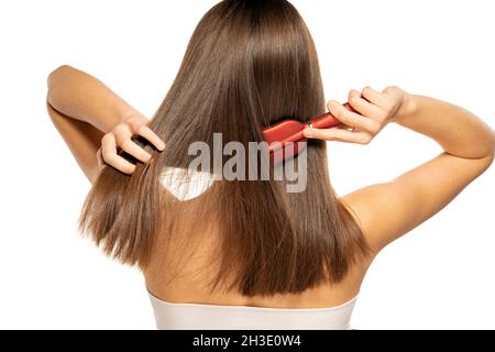 una vista posteriore di una donna spazzolando i capelli su uno sfondo bianco Foto Stock