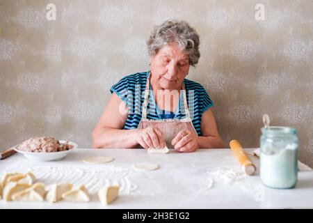 La nonna produce manti, scolpisce un piatto di pasta Foto Stock