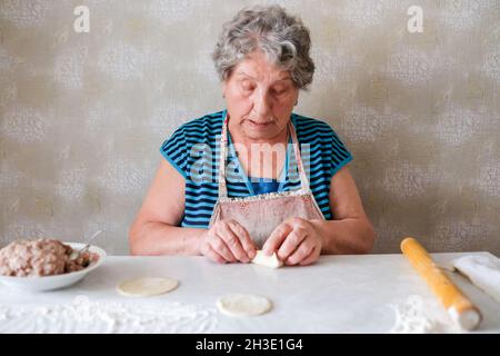 La nonna produce manti, scolpisce un piatto di pasta Foto Stock