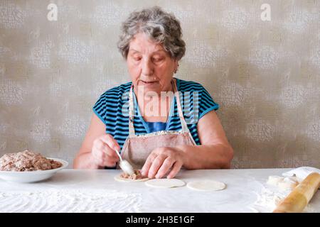 La nonna produce manti, mette la carne tritata su un pezzo di pasta rotonda con un cucchiaio Foto Stock