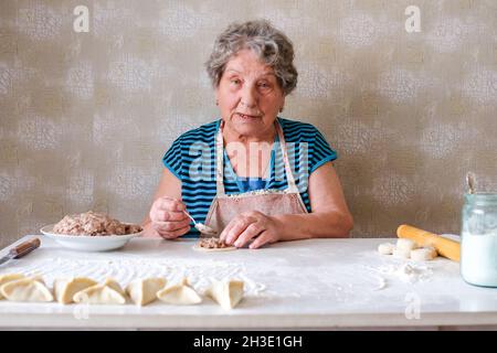 La nonna produce manti, mette la carne tritata su un pezzo di pasta rotonda con un cucchiaio Foto Stock