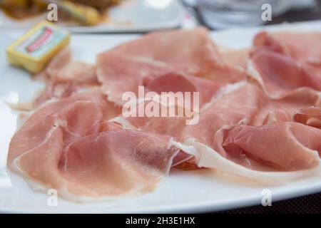 Prosciutto, prosciutto italiano secco, affettato a fette sottili e servito crudo in un piatto bianco Foto Stock