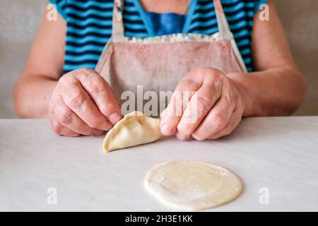 Una donna anziana scolpisce un piatto di pasta. Mani visibili Foto Stock