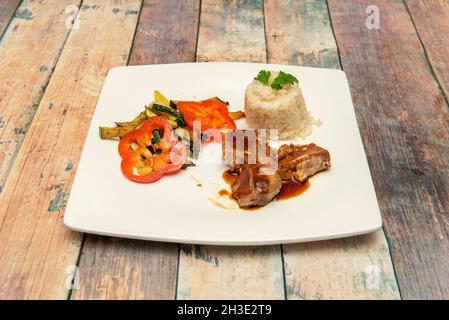 porzione di tonno stufato con guarnitura di verdure stufate e ciotola di riso bianco su tavola di legno Foto Stock