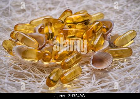 Le capsule di olio grasso di pesce Omega-3 si trovano sulle piccole conchiglie e sulla rete da pesca. EPA e DHA sono sostanze grasse essenziali di cui il nostro corpo ha bisogno ogni giorno Foto Stock