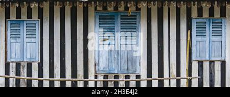 Vecchia casa grungy intempered con strisce bianche e nere sulle pareti e finestre in legno blu Foto Stock