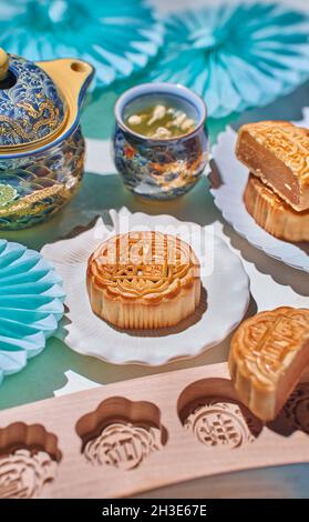 Dall'alto delle tradizionali mooncake con ripieno servito sul tavolo con stampi da forno vicino bollitore con tè alle erbe in camera luminosa Foto Stock